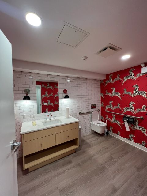 Restroom with wood vanity and red patterned wallpaper