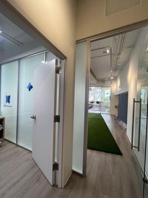 Glass partitions and an open door beside a corridor with a green turf strip