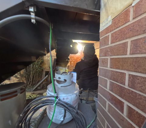 Welding in progress beneath a steel stair beside a brick wall