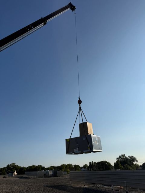Crane lifting HVAC unit above roofline